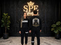 Man and woman wearing black #BLACKSHEEP sweatshirts and joggers on a city street